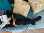 Black cable knit thigh high socks, lounging on a sofa with a book