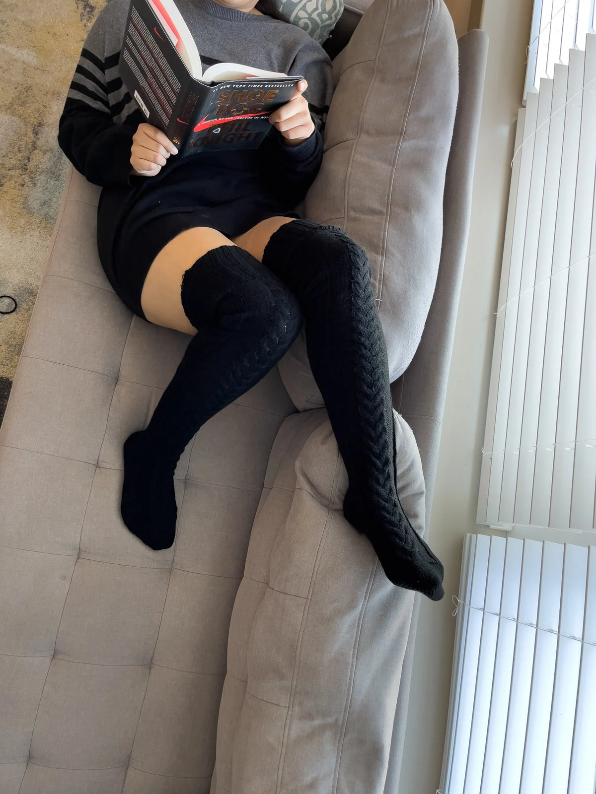 Black cable knit thigh high socks, worn while reading on a sofa