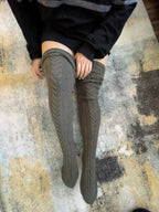 Charcoal cable knit thigh high socks, worn with a black sweater on a rug