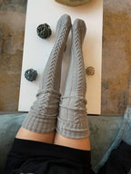 Gray cable knit thigh high socks, legs resting on a coffee table