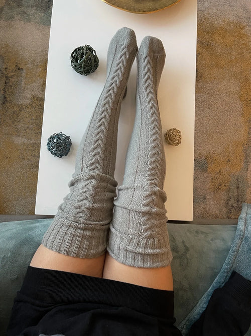 Gray cable knit thigh high socks, legs resting on a coffee table