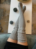 Gray cable knit thigh high socks, legs stretched on a coffee table