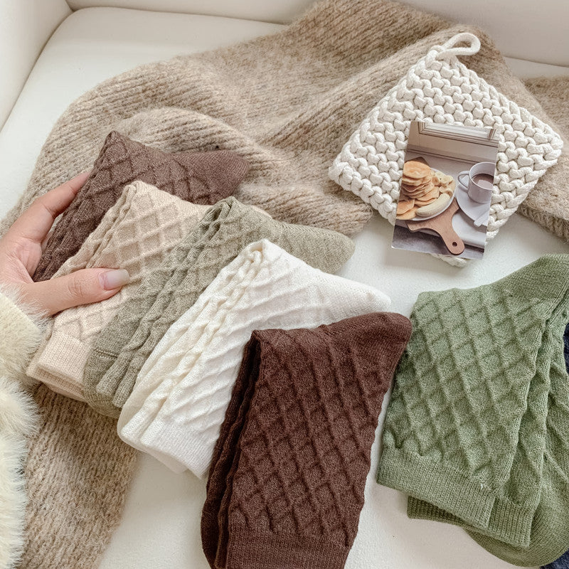 Checked knit crew socks in assorted colours, pairs stacked on a cozy blanket