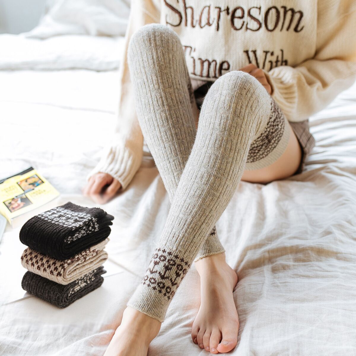 Light gray diamond cable knit thigh high socks, worn relaxing on a bed