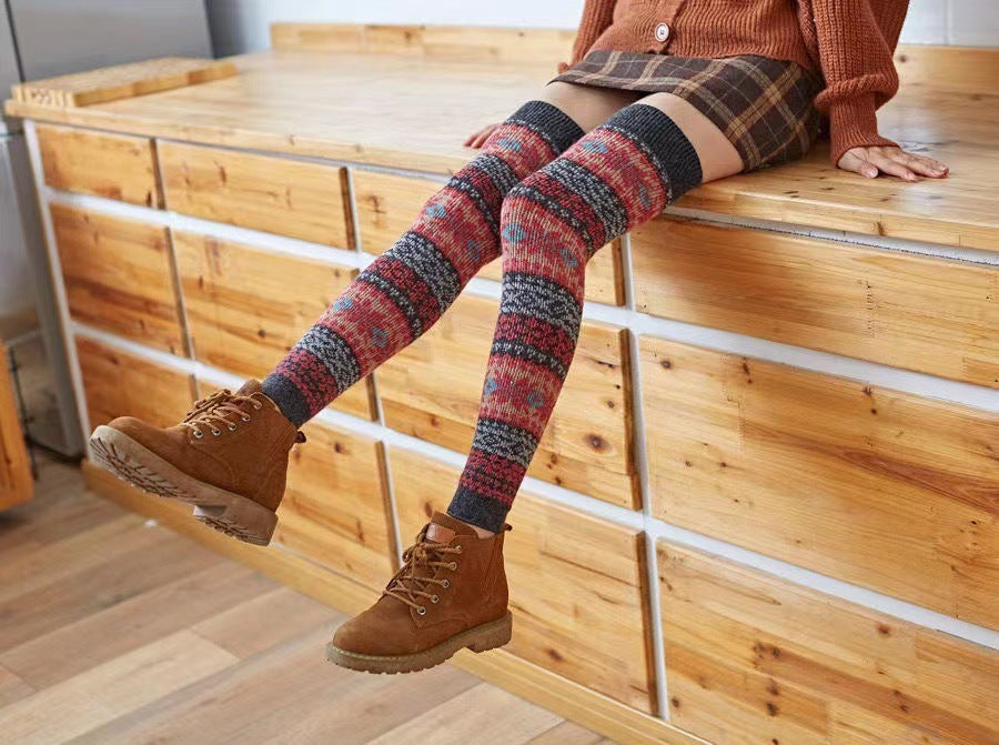 Dark gray fuzzy thigh high leg warmers, worn sitting on a wooden ledge