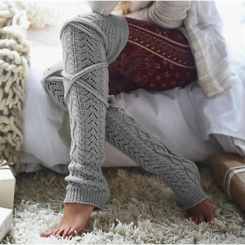 Light gray long cable knit leg warmers, worn sitting on a fluffy rug