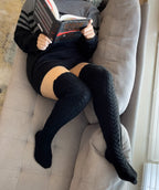 Black long knit over the knee socks, worn while reading on a sofa