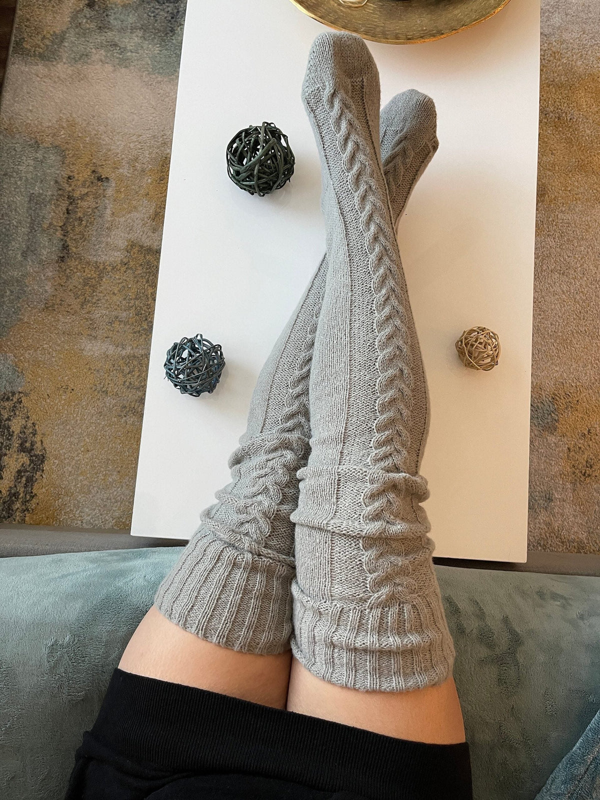 Gray long knit over the knee socks, legs resting on a coffee table