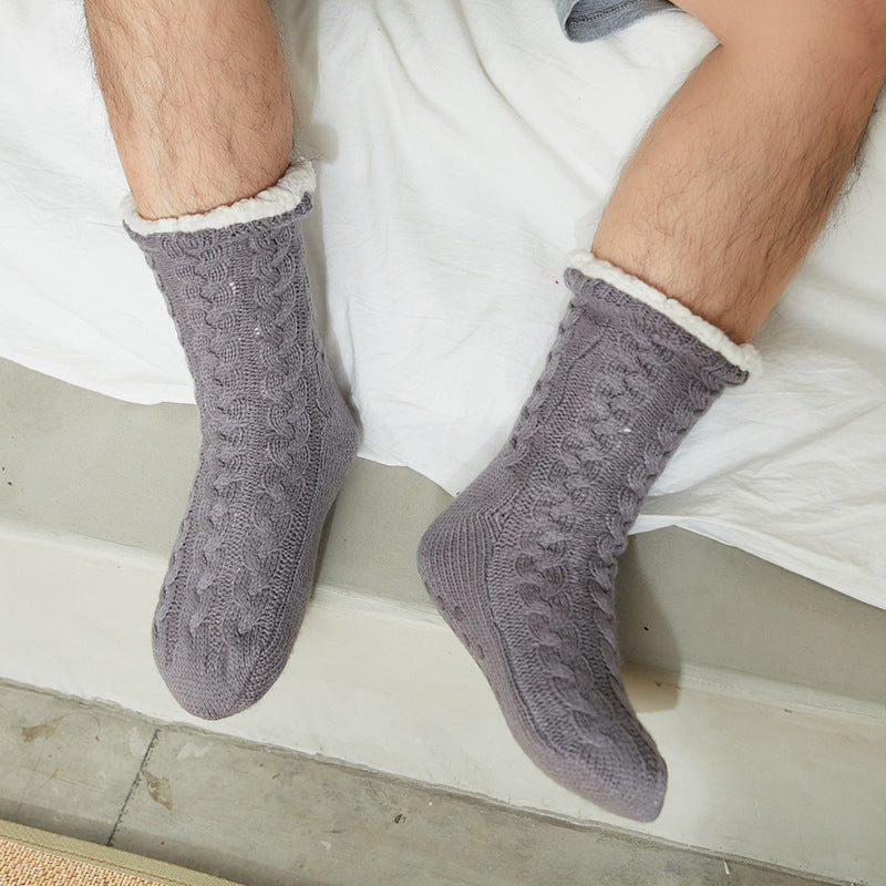 Gray men's fleece-lined slipper socks, worn sitting on a bed